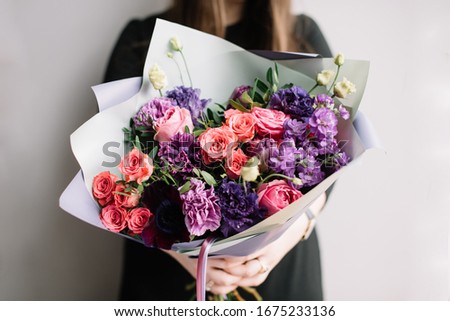 Very nice young woman holding big and beautiful bouquet of fresh roses, carnations, matthiola, eustoma flowers in purple and pink colors, cropped photo, bouquet close up 