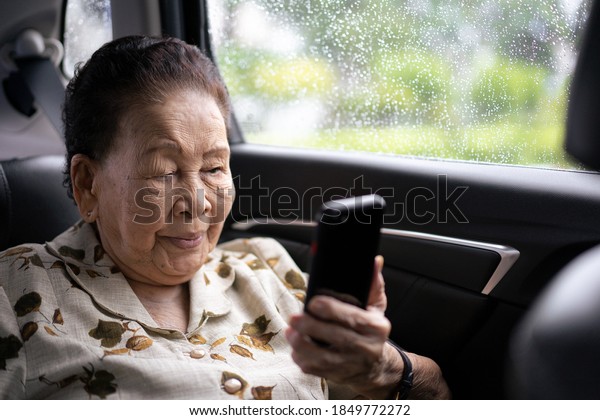 Very old\
Asian passenger woman age between 80 - 90 years old traveling by\
the car while raining and using a video call. Cheerful retired\
woman in a private car portrait with copy\
space