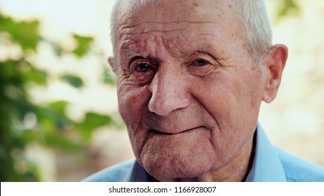 Very Old Man Portrait With Emotions. Grandfather Is Smiling And Looking To Camera. Portrait: Aged, Elderly, Senior. Close-up Of Old Man Sitting Alone Outdoors.