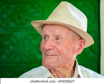 Very Old Man Portrait With Emotions. Grandfather Happy And Smiling. Portrait: Aged, Elderly Senior. Close-up Of A Pensive Old Man In White Hat Sitting Alone Outdoors At Summer.