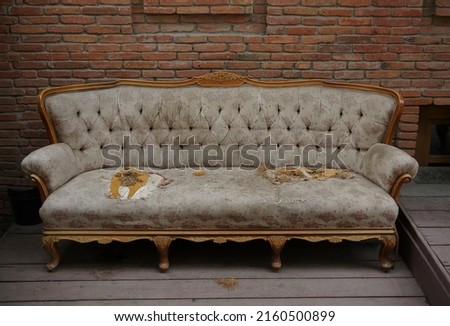 A very old ripped couch.  An old broken brown sofa needs repair. Large holes, springs, synthetic filler for furniture. Torn pillows, cut mattress. straw and foam rubber. red brick wall background. 
