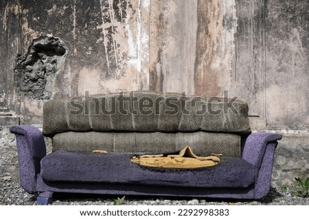 A very old ripped couch. An old broken brown sofa needs repair. Large holes, springs, synthetic filler for furniture. Torn pillows, cut mattress. straw and foam rubber. pink concrete wall background