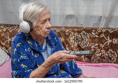 A Very Old Woman With Headphones Is Watching TV