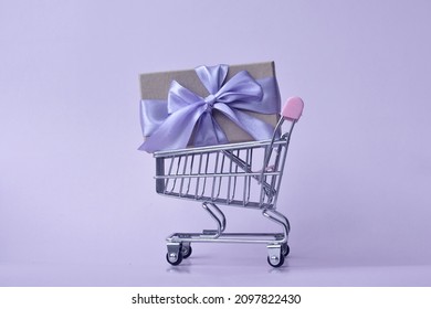 Very Peri Color. Kraft Gift Box Tied With Purple Ribbon In Shopping Cart. Zero Waste. Eco Friendly, No Plastic. Happy New Year. Merry Christmas. 8 March. Birthday. Present. Violet. Shopping. Sale