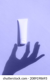 Very peri color of the year 2022. Trendy concept. Shadow hand gesture tube cosmetic. Natural skincare white beauty product on violet background. Facial skin treatment mockup.