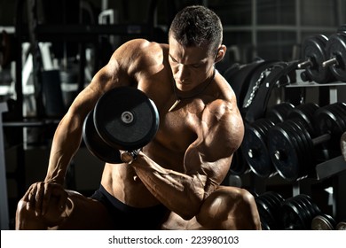 very power athletic guy bodybuilder ,  execute exercise with  dumbbells, in dark gym - Shutterstock ID 223980103