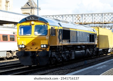 A very powerful freight train pulling it's loaded carriages past a station platform, in the United Kingdom.