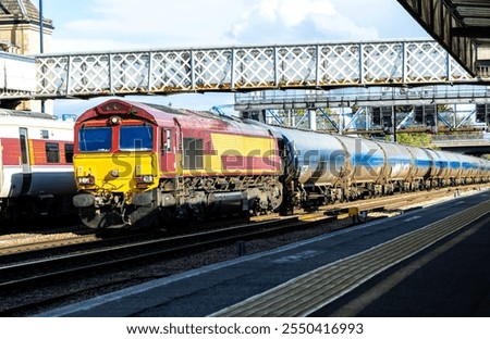 A very powerful freight train pulling it's loaded carriages past a station platform, in the United Kingdom.