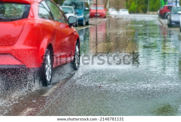 Very rainy day and car splashing water when\
passing through a puddle.