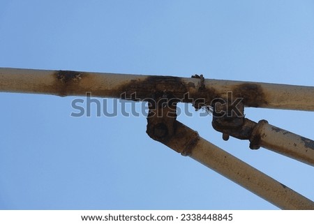 Very rusty piece of steel pipe with screws and bolts painted white using for hanging of merchant flags on the ship. As a background is a blue sky with copy space.