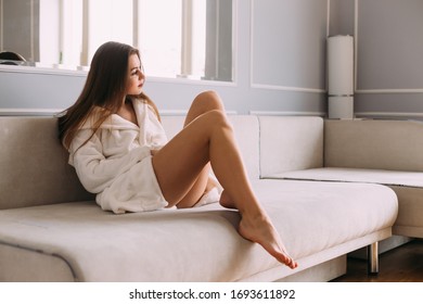 very sensual woman with white bathrobe and long hair in erotic pose lying on sofa