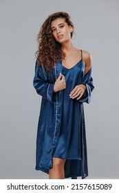 Very Sexy Curly Girl In A Blue Robe, Night Dress On A Gray Background. Home Clothes Concept. Catalog Photo