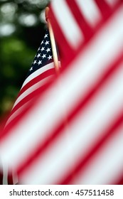 A Very Shallow Depth Of Field Focusing On A Small American Flag Hanging On A Flag Pole In The Background.  Blurred Out Stripes In The Foreground. Vertical Format With Copy Space