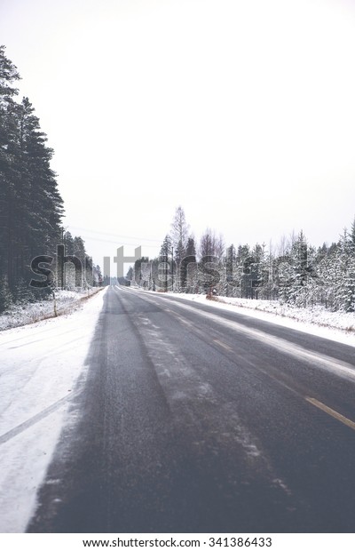 A very slippery road\
during winter. Black ice is covering the whole road and it is\
dangerous to drive even with studded winter tires. Image has a\
vintage effect applied.