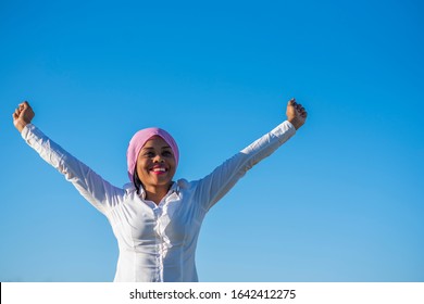 Very smiling African-American woman with a pink headscarf raising her arms - Shutterstock ID 1642412275