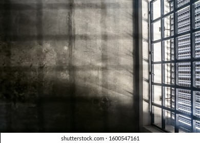 The very sober interior of a prison cell: barred windows with little light coming in and bare concrete walls. You should not want to be here