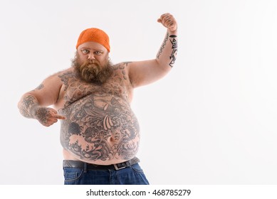 I am very strong. Fat bearded man is pointing finger at his big abdomen with proud. He is raising arm and showing muscle. Isolated and copy space in right side
