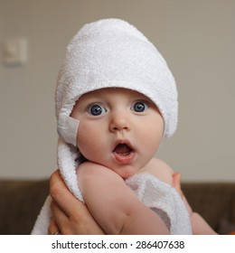 A very surprised baby, 6 months old, wrapped in a white towel.