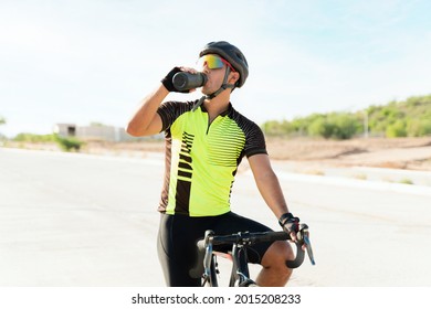 I'm very thirsty. Sporty young athlete drinking water from a bottle while resting and catching his breath on a bike. Professional cyclist hydrating - Powered by Shutterstock