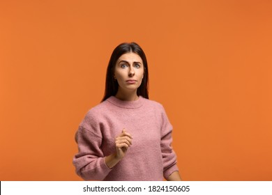Very unexpected. Photo of surprised woman looks at camera with eyes wide open, smirks face and has puzzled expression, tries to find out something, dressed in pink sweater, poses over vibrant orange