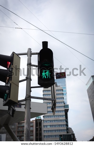 Very unusual green traffic light with people\
crossing the street handle and heart. Traffic light for pedestrians\
on the background of urban\
development
