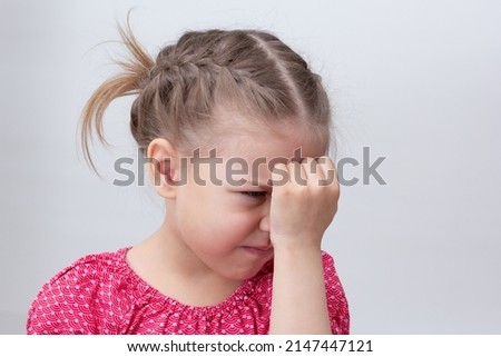 Very upset child holding fist on head on white background caucasian little girl 5-6 years in red looking down