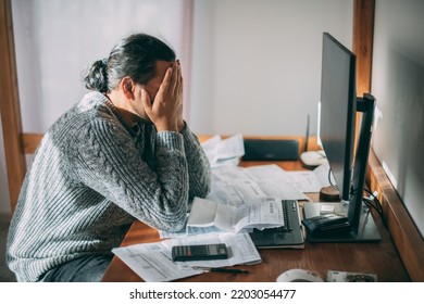 A Very Upset Man In A Warm Sweater Is Sitting At A Table With Utility Bills In His Hands.  A Man Emotionally Reacts To The Increased Costs Of Heating, Gas And Electricity Using A Calculator