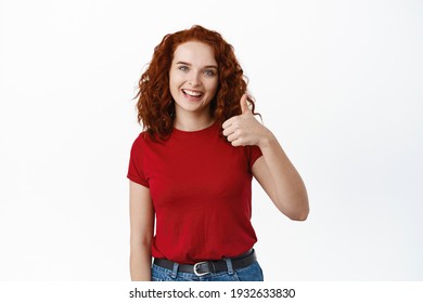 Very well. Portrait of positive redhead female student showing thumb up and smiling, nod in approval, say yes or alright, recommend product, approve and like it, white background - Shutterstock ID 1932633830