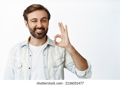 Very well. Smiling handsome man shows okay sign and winks, approves smth, give permission, recommends good product, white background.