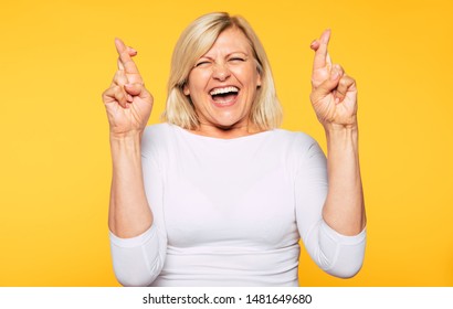 I very wish this stuff! Excited happy blonde senior woman is posing with crossing fingers isolated on yellow background