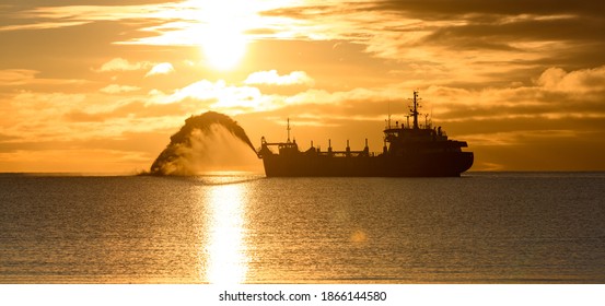 Vessel engaged in dredging at sunset time. Hopper dredger working at sea. Ship excavating material from a water environment. Beautiful sunset.