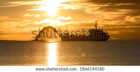 Vessel engaged in dredging at sunset time. Hopper dredger working at sea. Ship excavating material from a water environment. Beautiful sunset.