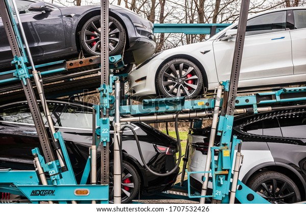 Vestal,\
NY/USA - April 11, 2020: A semi-tracker trailer hauling seven Tesla\
Models 3 and X, painted white, black and silver, sits parked\
overnight in a parking lot over Easter weekend.\
