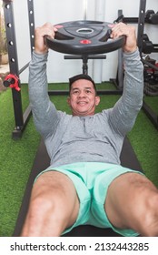 A Veteran Athlete Does Weighted Abdominal Crunches With A Plate While Lying On A Black Mat. Arms Raised For Added Difficulty. Working Out His Core At His Home Gym.