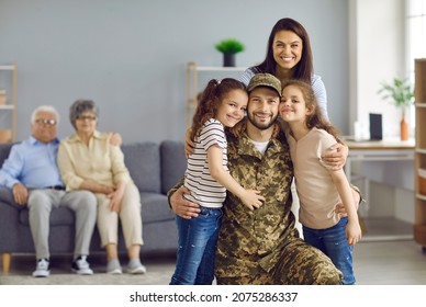 Veteran Soldier Comes Back To His Family From The Military. Happy Wife And Two Children Who Missed Daddy A Lot Hugging Him And Looking At Camera On Blurred Copy Space Home Background With Grandparents