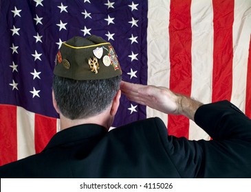 A Veteran Wearing A Decorated Cap, Saluting The American Flag.