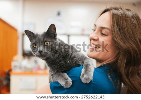 Veterinary professional smiling while holding a grey cat in a clinic setting