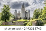 Veves Castle on hill with stormy gray sky in background, surrounded by green leafy trees, stone building with its towers with conical roofs, sunny day in Houyet, Namur province, Wallonia, Belgium