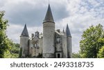 Veves Castle with stone walls with its towers with conical roofs, surrounded by green leafy trees, stormy gray sky in background, sunny day in Houyet, Namur province, Wallonia, Belgium