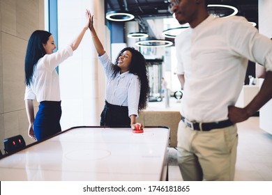 Vexed African American Man With Hands Aside Looking At Air Hockey Table While Cheerful Multiethnic Women Giving High Five In Honor Of Victory  