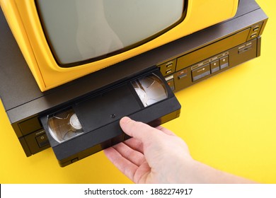 VHS videocassette is put into the video recorder to watch the video. Old yellow vintage TV with VCR and videotape on black background from 1980s, 1990s, 2000s. 