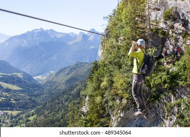 Via Ferrata Climbing, Woman In Harness Crossing Rope Bridge In The Mountains, Alpinism Or Extreme Sport