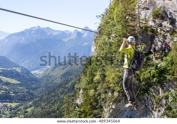 via ferrata\
climbing, woman in harness crossing rope bridge in the mountains,\
alpinism or extreme sport