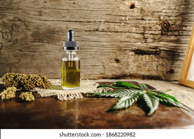 a vial with a dropper of cannabis concentrate cbd stands next to dried marijuana buds and a cannabis leaf on a rusty wooden and sackcloth background. copy space