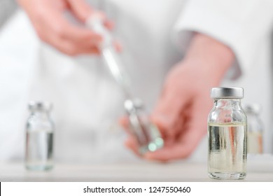 Vial Of Medicine On Blurred Background Of A Medical Worker Filling A Syringe. New Vaccine, Breakthrough In Medicine.