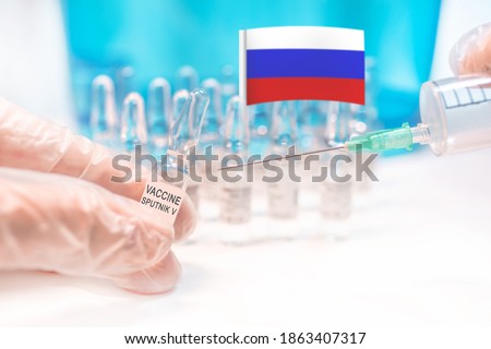 A vial with Russian anti covid-19 (Sars-CoV-2) vaccine called Sputnik V (Gam-COVID-Vac, trade-named Sputnik V) with a syringe and a Russian flag in a background