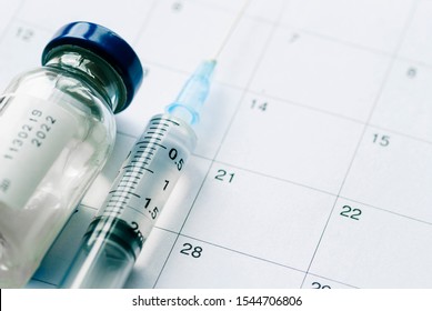 The Vial With Vaccine And Syringe On Calendar Background, As A Concept Of Vaccination Season And Date. Viewed From Above With Copy Space