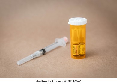 Vials of Naloxone in an orange plastic prescription bottle and syringe in front of seamless plain background