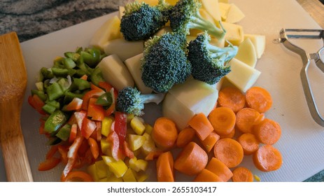 A vibrant array of fresh, chopped vegetables including broccoli, bell peppers, carrots, and potatoes on a cutting board, ready for cooking.