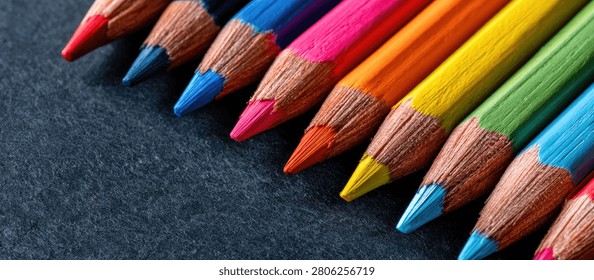 A vibrant array of sharpened colored pencils arranged diagonally on a dark, textured background, showcasing their tips and wooden barrels.